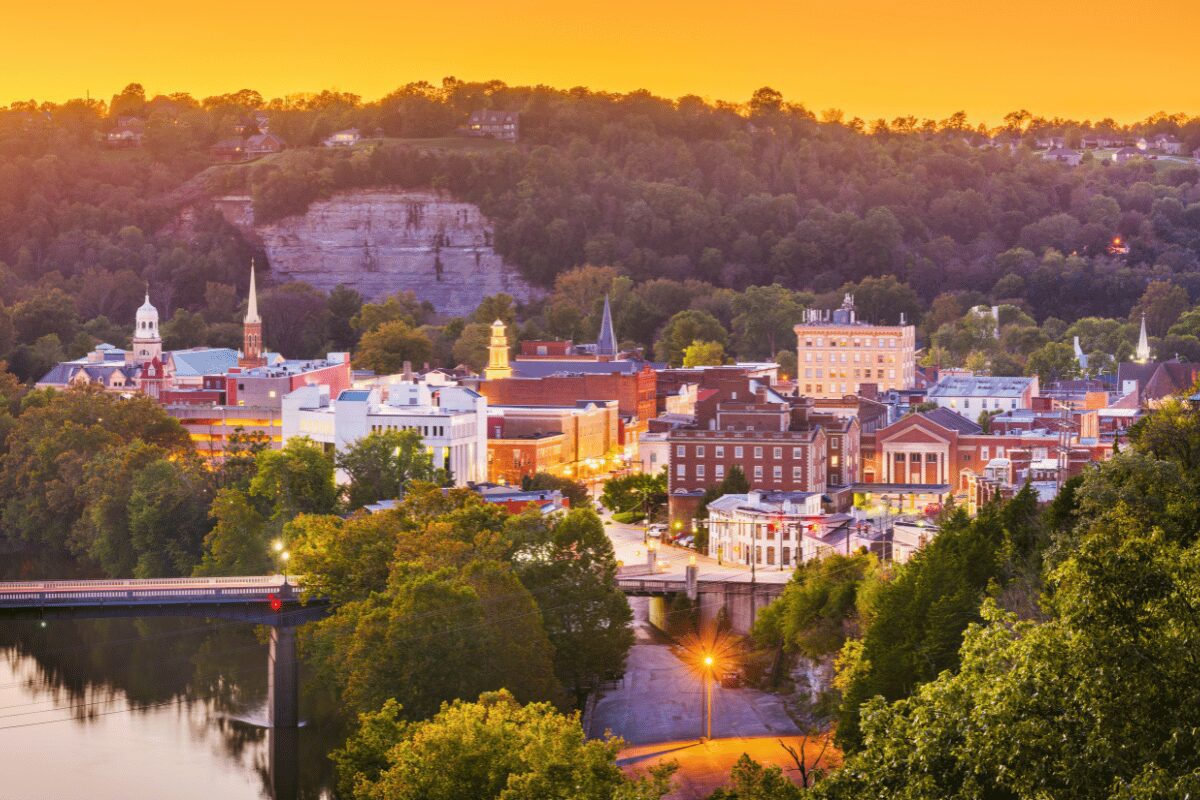 Downtown Frankfort, Kentucky, at sunset with historic brick buildings, church steeples and a riverfront bridge.