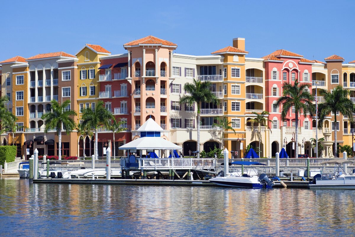 Colorful waterfront buildings in Naples, Florida, with tile roofs, balconies, palm trees and marina docks.