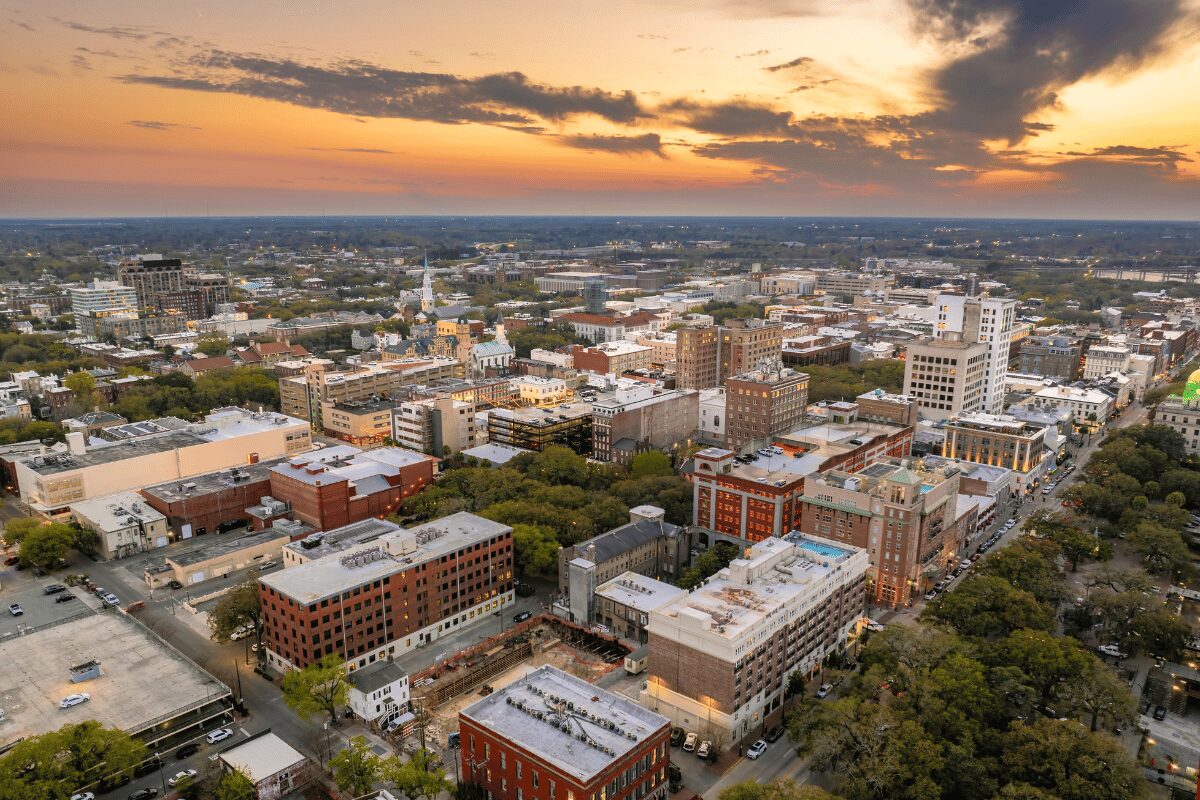 Aerial view of downtown Savannah, Georgia, at sunset with historic buildings, commercial rooftops and tree-lined streets.