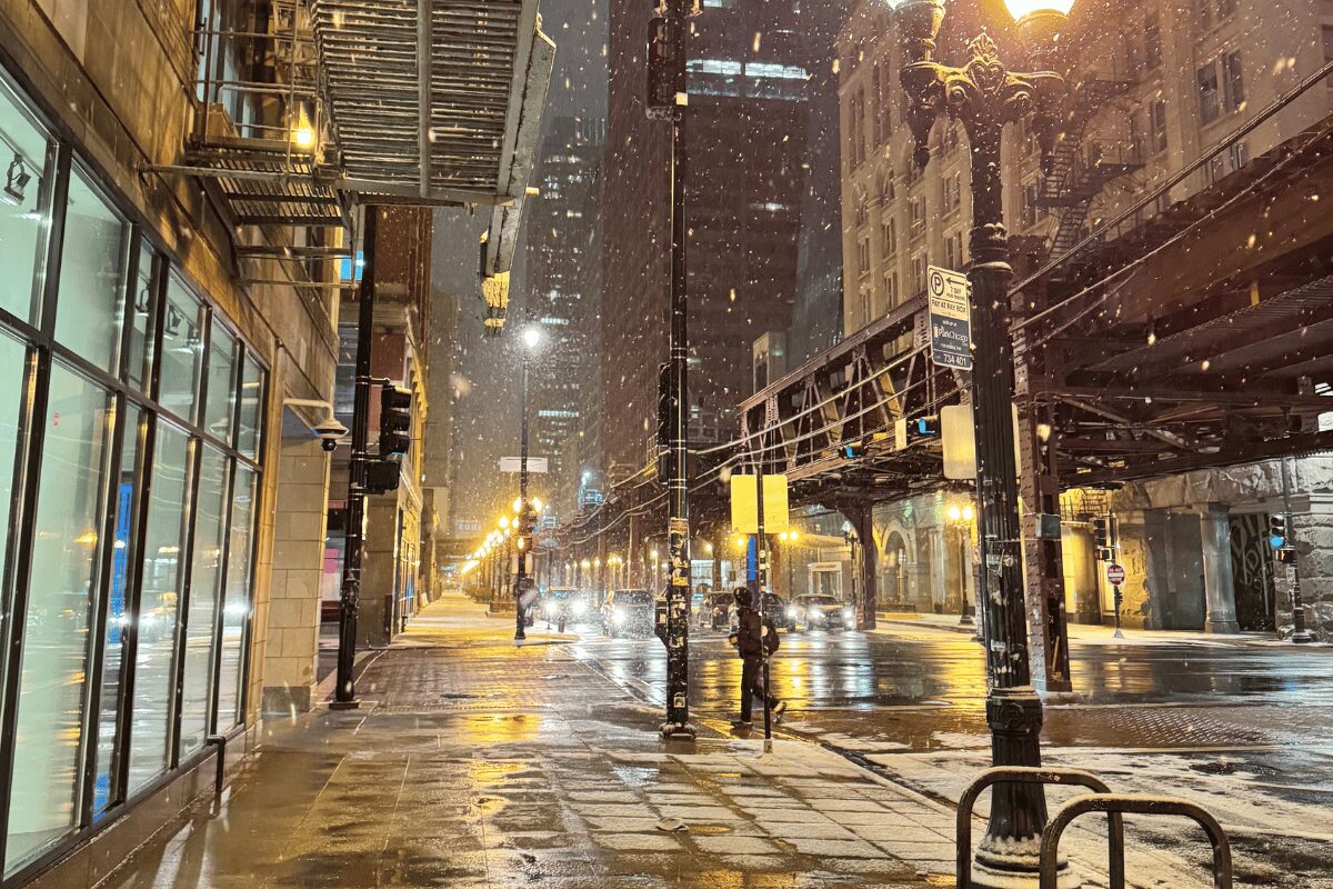 Winter snowfall along a downtown Chicago, Illinois, street with commercial storefronts and elevated train tracks.