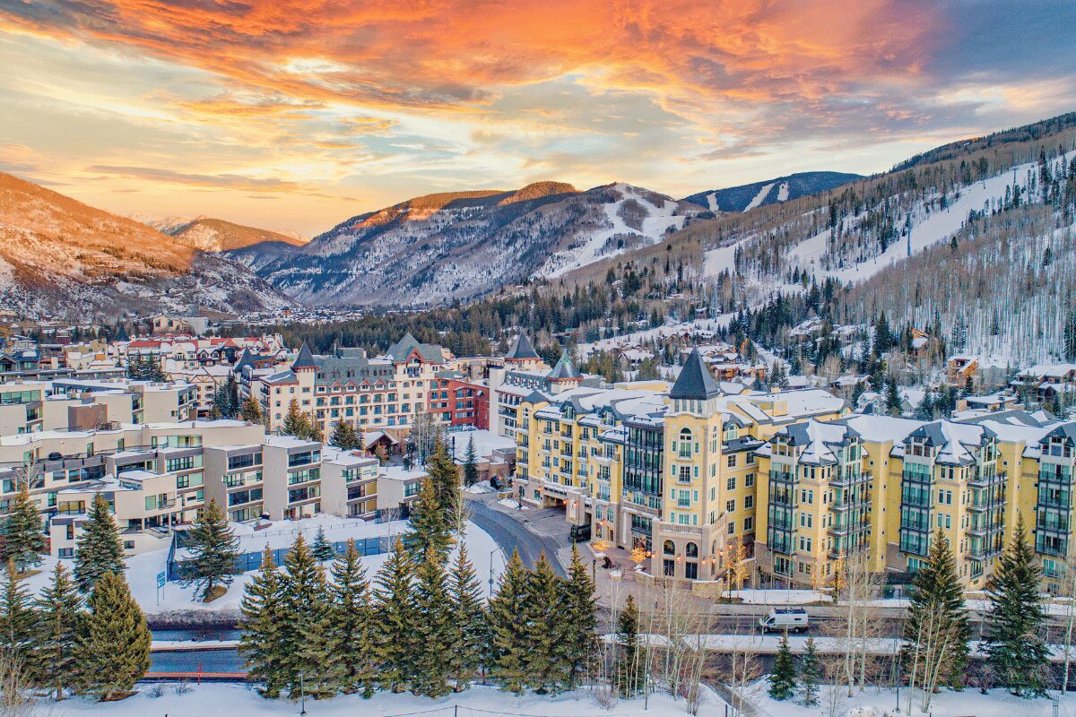 Snow-covered hotels and resort buildings in Vail, Colorado, with mountain ski slopes in the background.