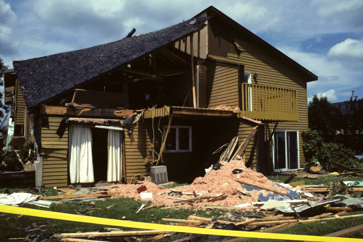 Tornado-damaged two-story building with a partially collapsed roof, missing exterior walls, exposed insulation and scattered debris.